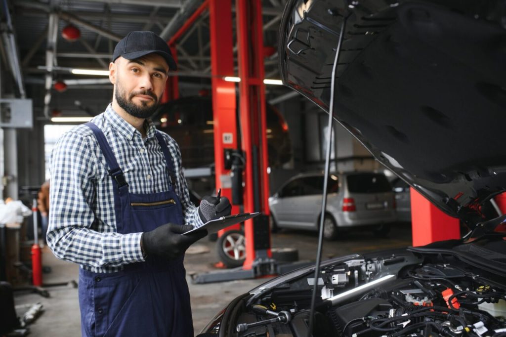 handsome car mechanic is posing in a car service e1696422104185